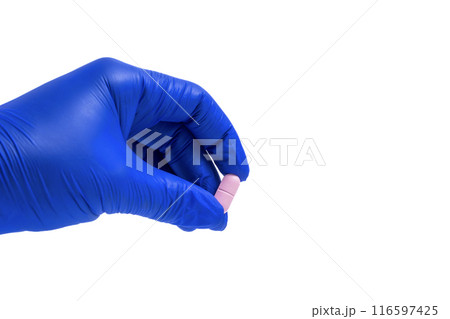 Hand in a blue glove holding a pink pill isolated on white background. Closeup 116597425