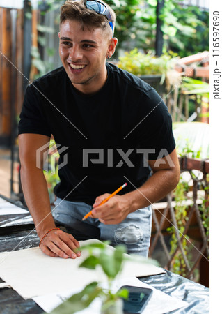 Young man smiling during a fine arts class work with his classmates. Vertical Young man smiling during a fine arts class work with his classmates. Vertical 116597690