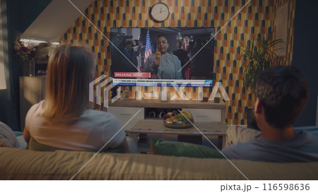 Couple watches news about United States elections on TV screen sitting on sofa 116598636