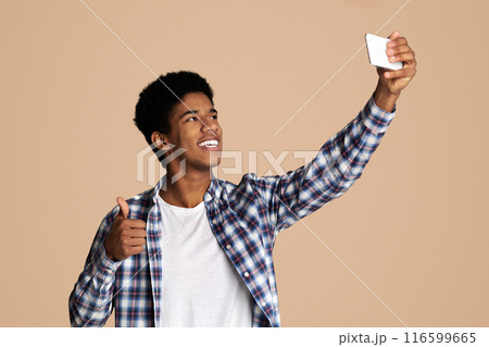 Happy teen guy making selfie and showing thumb up, white studio background Happy teen guy making selfie and showing thumb up, white studio background 116599665