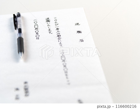 白いテーブルに置かれた手書きの退職届とゲルインクの黒ペン 116600216