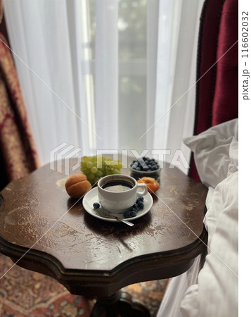 Cup of coffee with fresh fruits on the bedside table in a hotel room with red curtains Cup of coffee with fresh fruits on the bedside table in a hotel room with red curtains 116602032