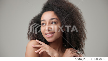 Beauty and healthcare concept - beautiful African American woman with curly afro hairstyle and clean, healthy skin touching face with hand, doing facial massage, posing and looking at camera 116603892