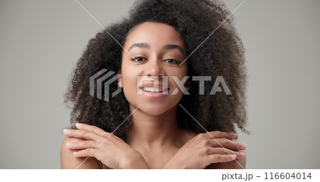 Beauty and healthcare concept - beautiful African American woman with curly afro hairstyle and clean, healthy skin touching face with hand, doing facial massage, posing and looking at camera Beauty and healthcare concept - beautiful African American woman with curly afro hairstyle and clean, healthy skin touching face with hand, doing facial massage, posing and looking at camera 116604014