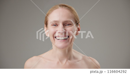 Real people - concept of age, beauty, health and dry skin care - beautiful mature Caucasian middle-aged woman in her 50s looks with a calm confident look at the camera, smiles a bright toothy smile 116604292