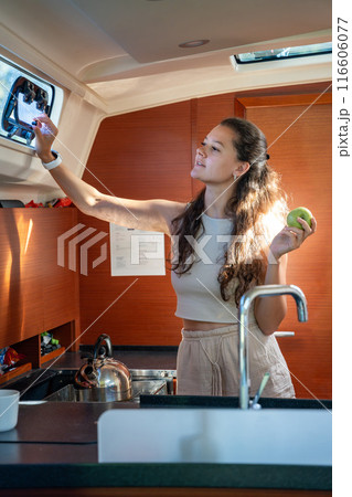Young woman standing in kitchen in cabin of modern yacht during sailing in sea. Yacht life concept Young woman standing in kitchen in cabin of modern yacht during sailing in sea. Yacht life concept 116606077