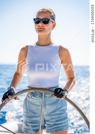 Young woman female captain stands at the helm and controls a sailboat during a journey by sea Young woman female captain stands at the helm and controls a sailboat during a journey by sea 116606088