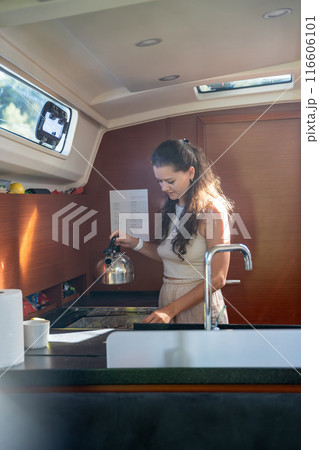 Young woman standing and preparing tea in kitchen in cabin of modern yacht during sailing in sea. Yacht life concept 116606101