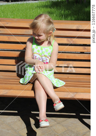 Little girl laughing while sitting on bench in city park. Positive children's emotions. Little girl laughing while sitting on bench in city park. Positive children's emotions. 116607778