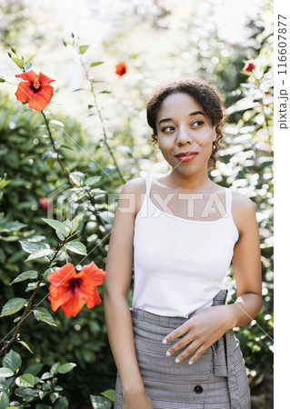 Young Woman in Garden with Red Hibiscus Flowers Enjoying Nature on a Sunny Day 116607877
