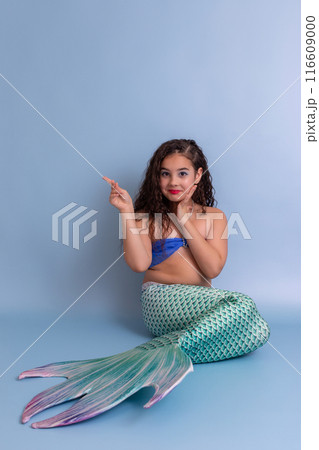 A happy girl in a mermaid costume sits on a blue background 116609000