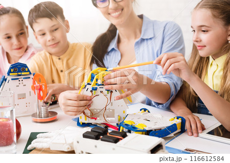 A teacher guides a group of children as they work together to build a robot. The students are focused and engaged, learning about STEM concepts through hands-on experience. A teacher guides a group of children as they work together to build a robot. The students are focused and engaged, learning about STEM concepts through hands-on experience. 116612584