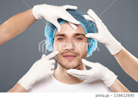 Aesthetic Cosmetology concept. Doctor's hands in gloves touching face of handsome young man, closeup 116612695