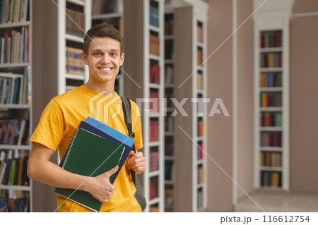 Knowledge. Excited caucasian male student posing next to bookshelves in campus library, empty space Knowledge. Excited caucasian male student posing next to bookshelves in campus library, empty space 116612754