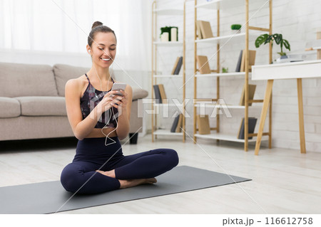 Exercising at home. Woman having rest, using smartphone and listening music Exercising at home. Woman having rest, using smartphone and listening music 116612758