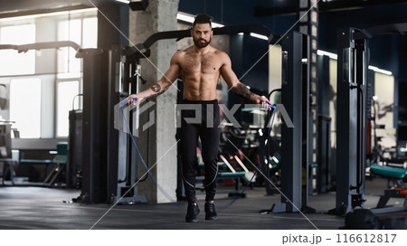 Best cardio workout. Sporty muscular man with perfect body training with skipping rope in gym interior, free space 116612817