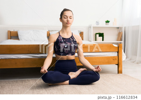 Healthy lifestyle. Young woman exercicing in lotus position, sitting on floor in bedroom, free space Healthy lifestyle. Young woman exercicing in lotus position, sitting on floor in bedroom, free space 116612834