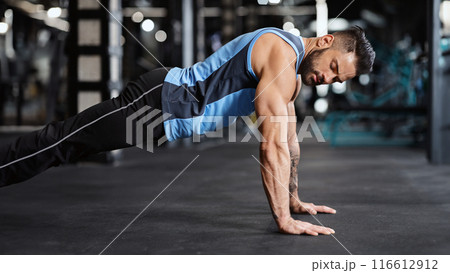Sporty young man doing pushups in gym, side view, free space 116612912