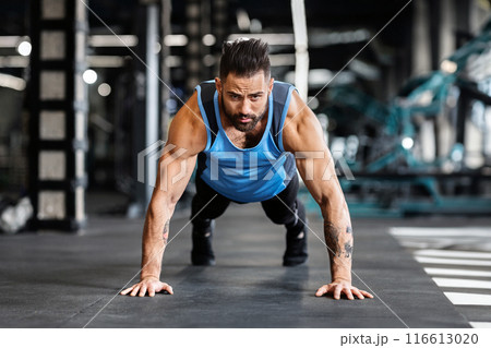 Concentrated muscular guy training in gym, doing push up exercises, free space 116613020