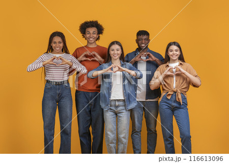This photo features five diverse young adults making heart shapes with their hands. They are standing in a row in front of a bright yellow background 116613096