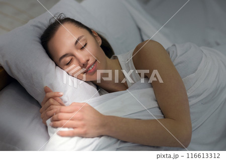 Pleasant dream. Girl sleeping in bed, morning sunbeam falling on face 116613312