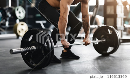 Hard strength workout. Muscular powerlifter lifting heavy barbell from gym floor, empty space 116613569