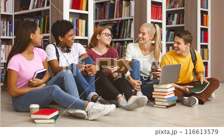 Group of international tennage friends having conversation while preparing for school exams, library interior, free space Group of international tennage friends having conversation while preparing for school exams, library interior, free space 116613579