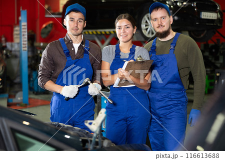 Two guys and woman mechanics posing at car service station 116613688