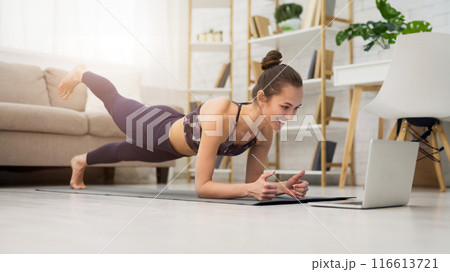 Fitness girl training yoga, watching online videos on laptop in the living room at home 116613721