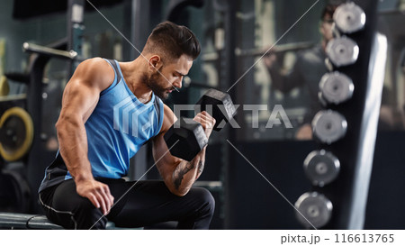 Bodybuilder pumping his biceps with dumbbell in gym, empty space Bodybuilder pumping his biceps with dumbbell in gym, empty space 116613765