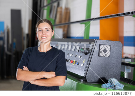Smiling female glass workshop worker standing near industrial line 116613877