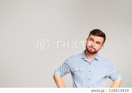 Thoughtful young bearded man wearing casual shirt looking away at copy space on grey studio background 116613919