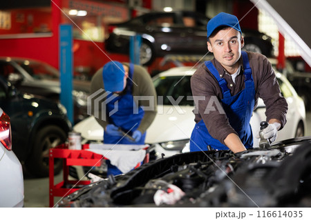 Skilled male auto mechanic in blue overalls repairing automobile 116614035