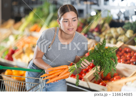 Young girl purchaser buying organic carrot in grocery store 116614085