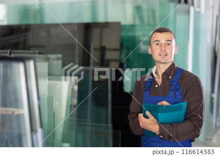 Experienced worker checks the quality of made window glass in an industrial workshop, marks the data in documents 116614383
