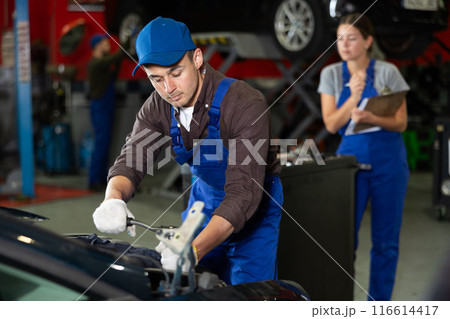 Young guy mechanic repairs car in car service station Young guy mechanic repairs car in car service station 116614417