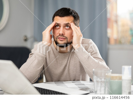 Young man having headache while sitting at home table with laptop 116614456