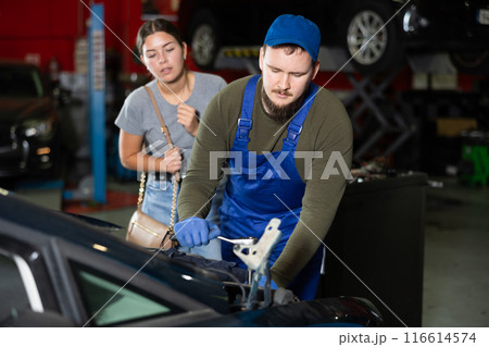Girl watches car mechanic repairing her car in car service center Girl watches car mechanic repairing her car in car service center 116614574