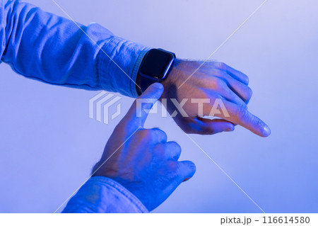 Man interacts with their smartwatch, using their finger to navigate through notifications or options. The ambient blue light gives the scene a futuristic and modern feel, cropped Man interacts with their smartwatch, using their finger to navigate through notifications or options. The ambient blue light gives the scene a futuristic and modern feel, cropped 116614580