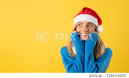 A woman wearing a red Santa hat and a cozy blue sweater, looking festive and ready for the holiday season. She stands against a neutral background, bringing a touch of Christmas spirit to the scene. 116614600