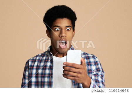 Wow. Shocked african guy checking social networks on phone over white background Wow. Shocked african guy checking social networks on phone over white background 116614648