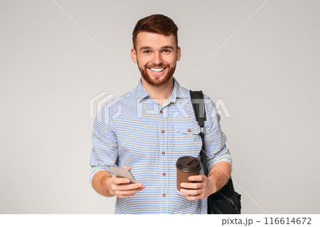 Have a good day. Cheerful man holding cup of coffee and using phone on studio background, copy space 116614672
