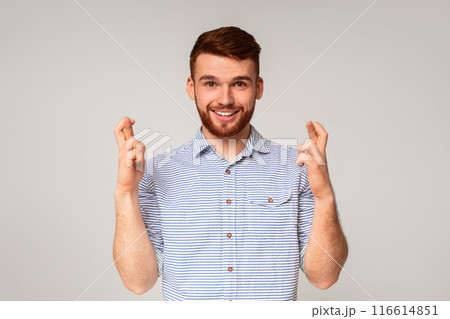 Positive millennial bearded stylish guy crossing fingers and making wish on beige studio background Positive millennial bearded stylish guy crossing fingers and making wish on beige studio background 116614851