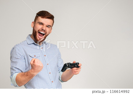 Victory taste. Young bearded guy win video game and feel happy on grey studio background, free space 116614992