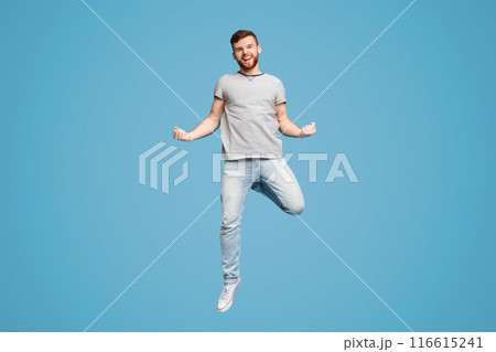 Celebrating Success. Excited Young Millennial Redhaired Man Jumping And Gesturing On Blue Studio Background 116615241