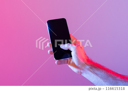A person holds a smartphone with a dark, unlit screen against a gradient purple background. The lighting casts a soft, ambient glow, creating a modern and tech-savvy atmosphere. A person holds a smartphone with a dark, unlit screen against a gradient purple background. The lighting casts a soft, ambient glow, creating a modern and tech-savvy atmosphere. 116615318