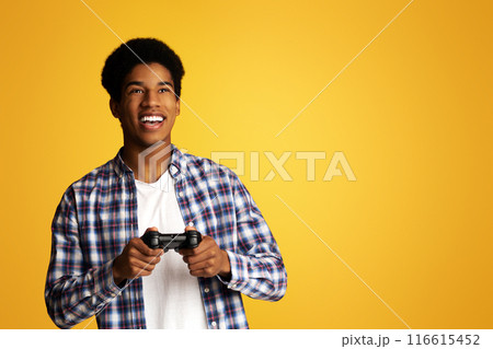 Gambling Addiction. Excited Guy Holding Joystick and Playing Video Games, Yellow Background 116615452