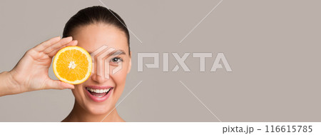 Pretty young woman holding orange half over her eye and smiling, colorful studio background, panorama with copy space Pretty young woman holding orange half over her eye and smiling, colorful studio background, panorama with copy space 116615785