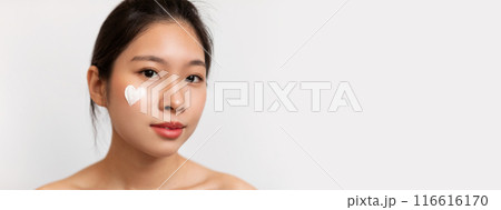 Closeup portrait of pretty korean lady with moisturizer cream on her face in heart shape, woman testing new beauty product, white studio background. Face care concept, copy space 116616170