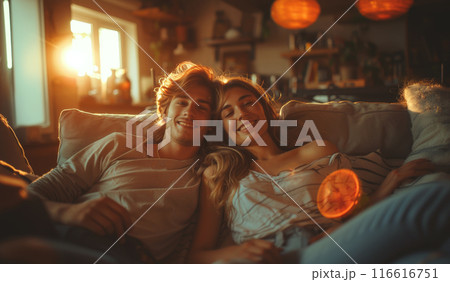 A young couple relaxes on a couch together, bathed in the warm glow of the setting sun. 116616751